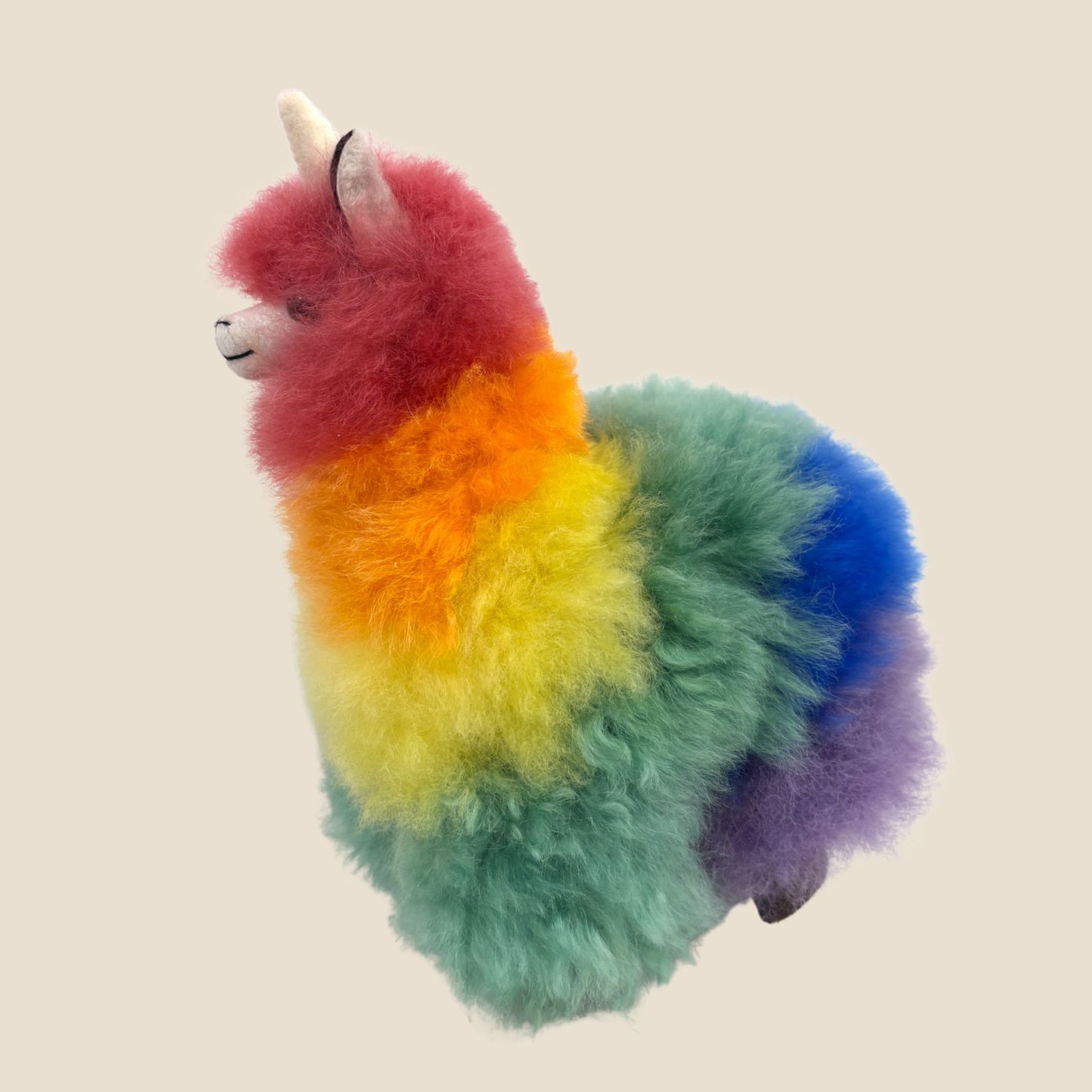 Colorful plush toy resembling a alpaca with a unicorn horn on a beige background