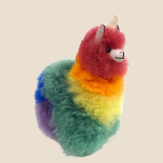 Colorful plush toy resembling a alpaca with a unicorn horn on a beige background