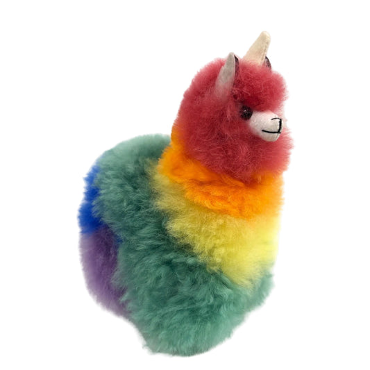 Colorful plush toy resembling a alpaca with a unicorn horn on a beige background