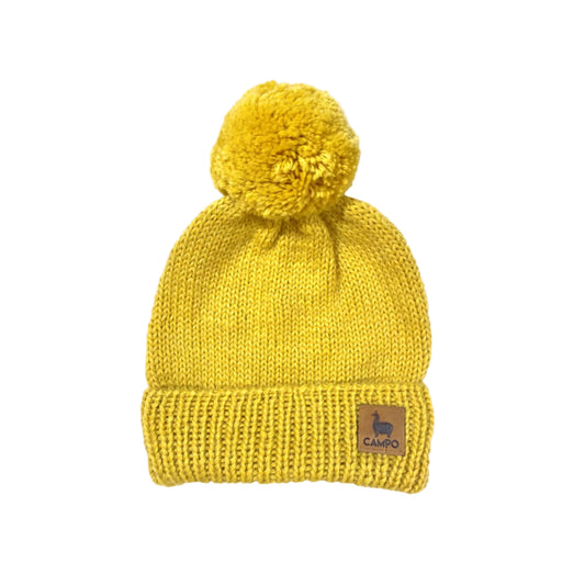 Mustard knit beanie with pom-pom on a beige background