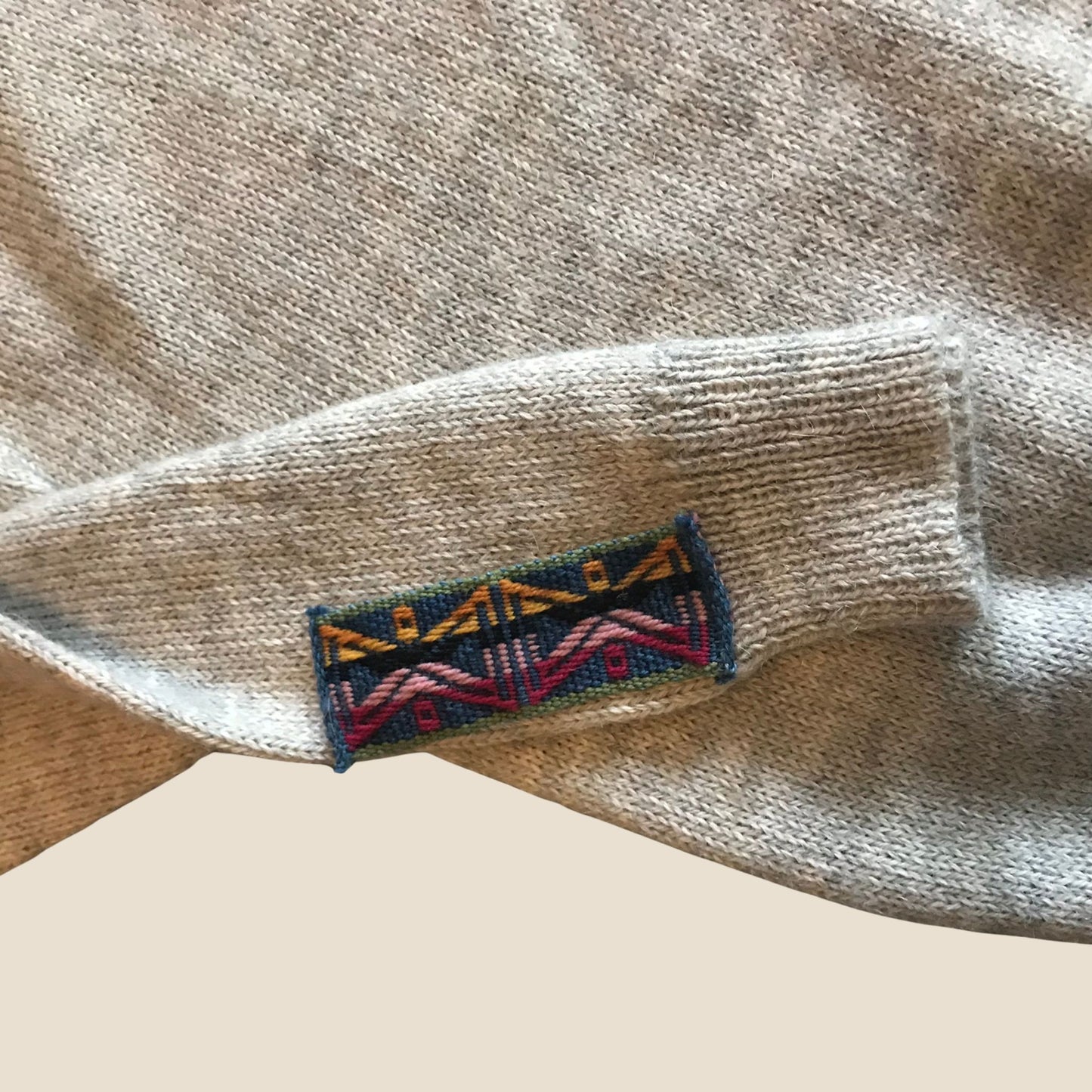 Close-up of a brand label on a beige sweater sleeve.