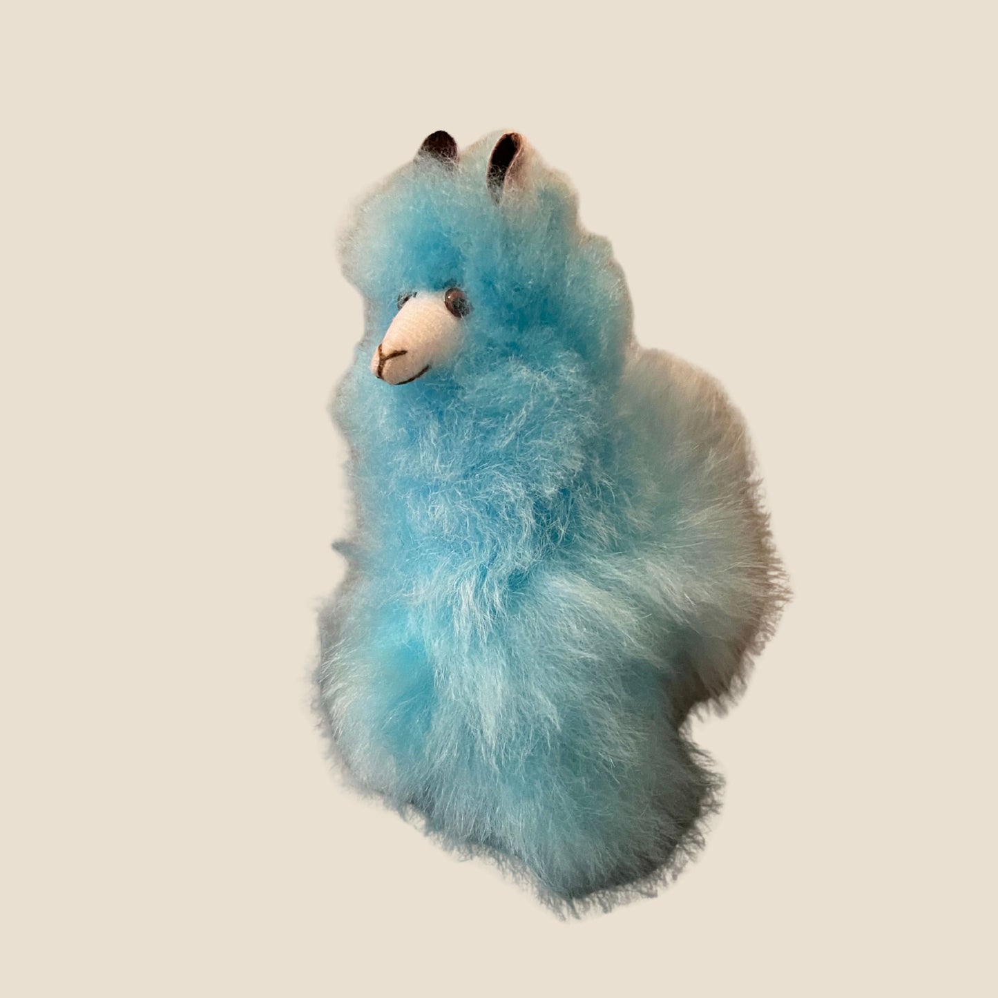 Blue plush alpaca toy on a beige background