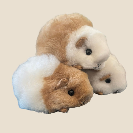 Three plush toy guinea pigs on a beige background