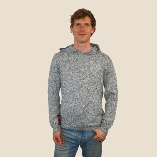 Man wearing a gray hooded sweater and blue jeans on a beige background