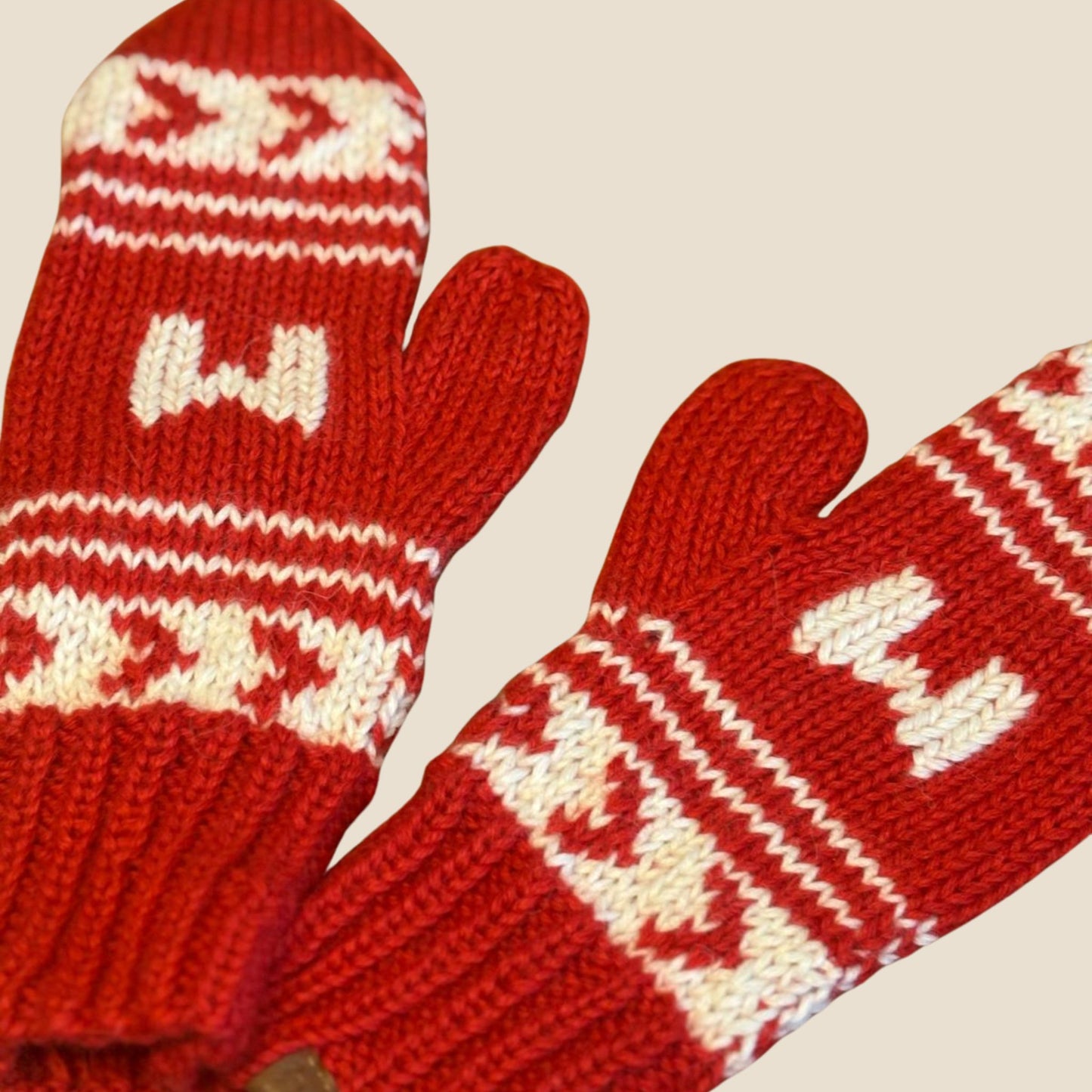 Red knitted mittens with white pattern on a beige background