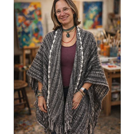 Woman wearing a gray shawl in an art studio with paintings and art supplies in the background