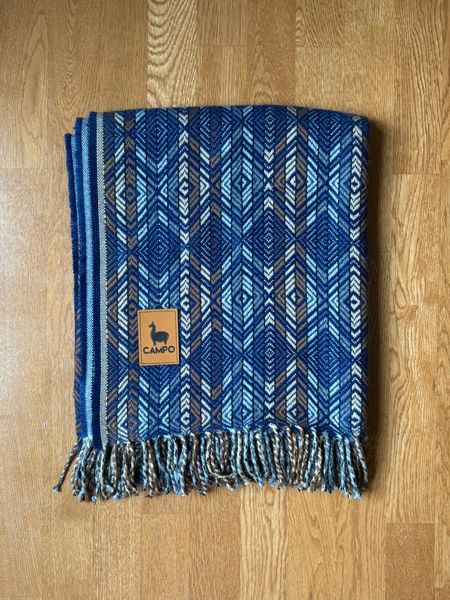 Blue Natural woven blanket with a brand logo on a wooden surface