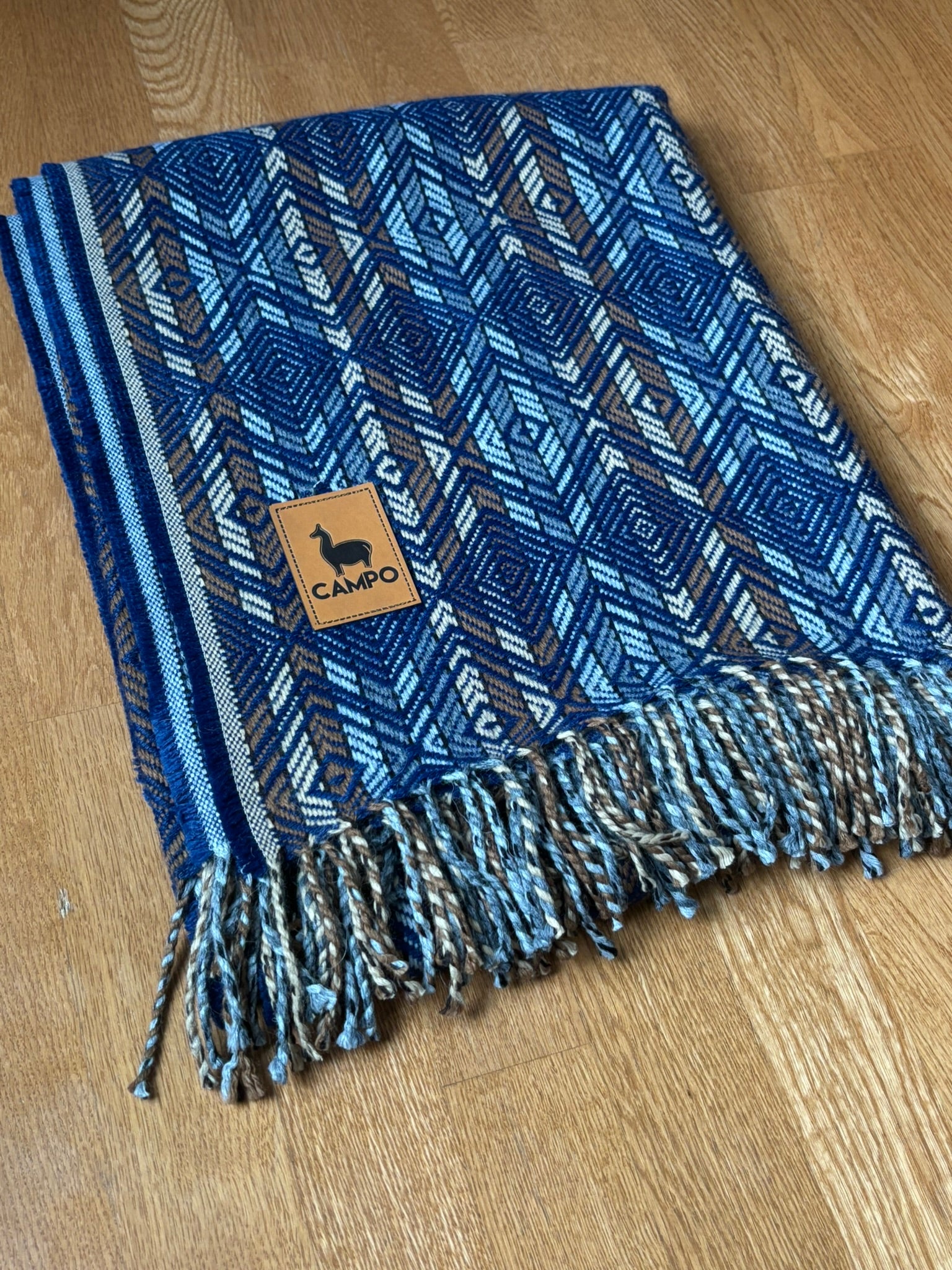 Blue natural woven blanket with a brand logo on a wooden surface