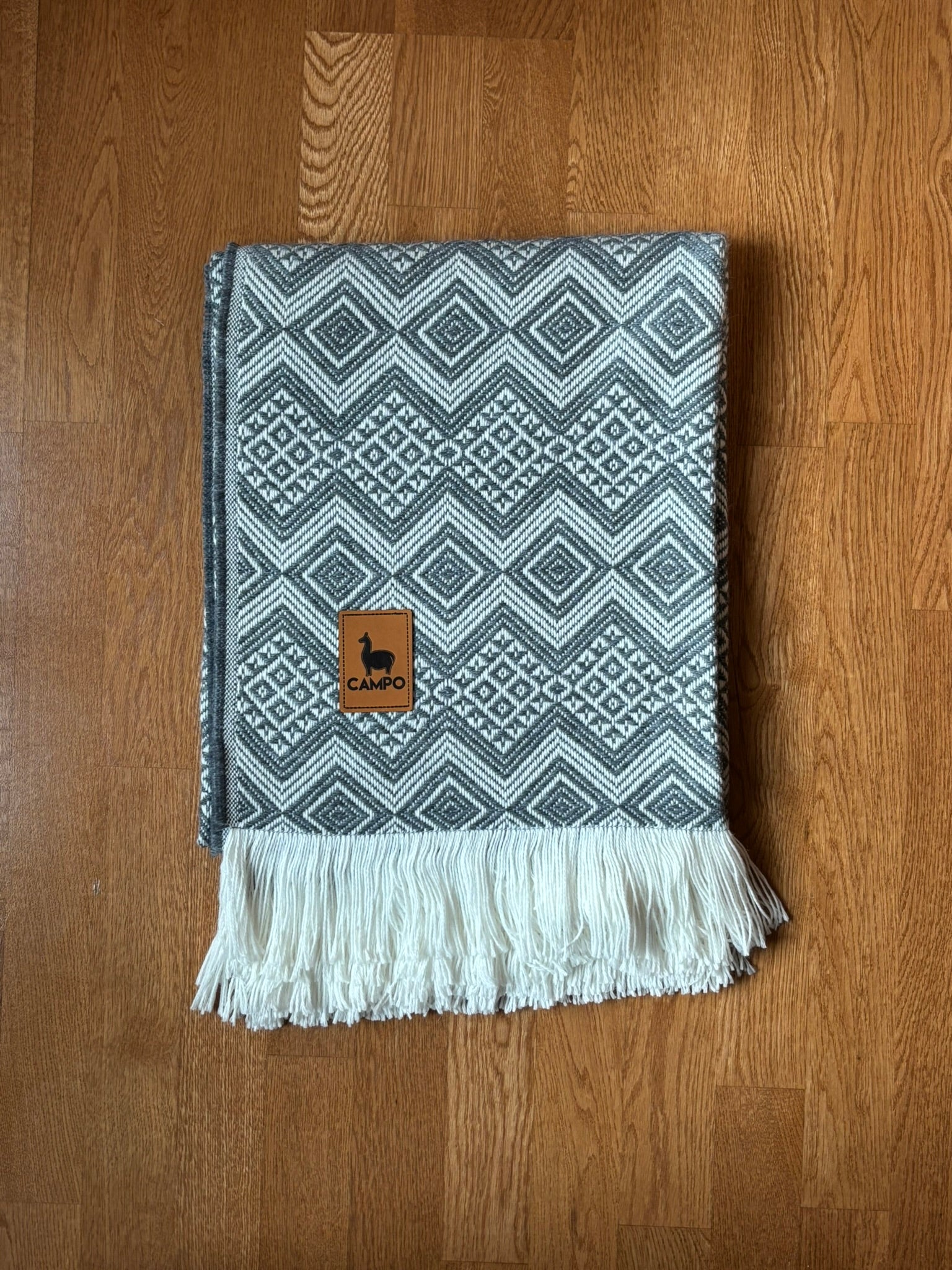 Silver woven blanket with a brand logo on a wooden surface