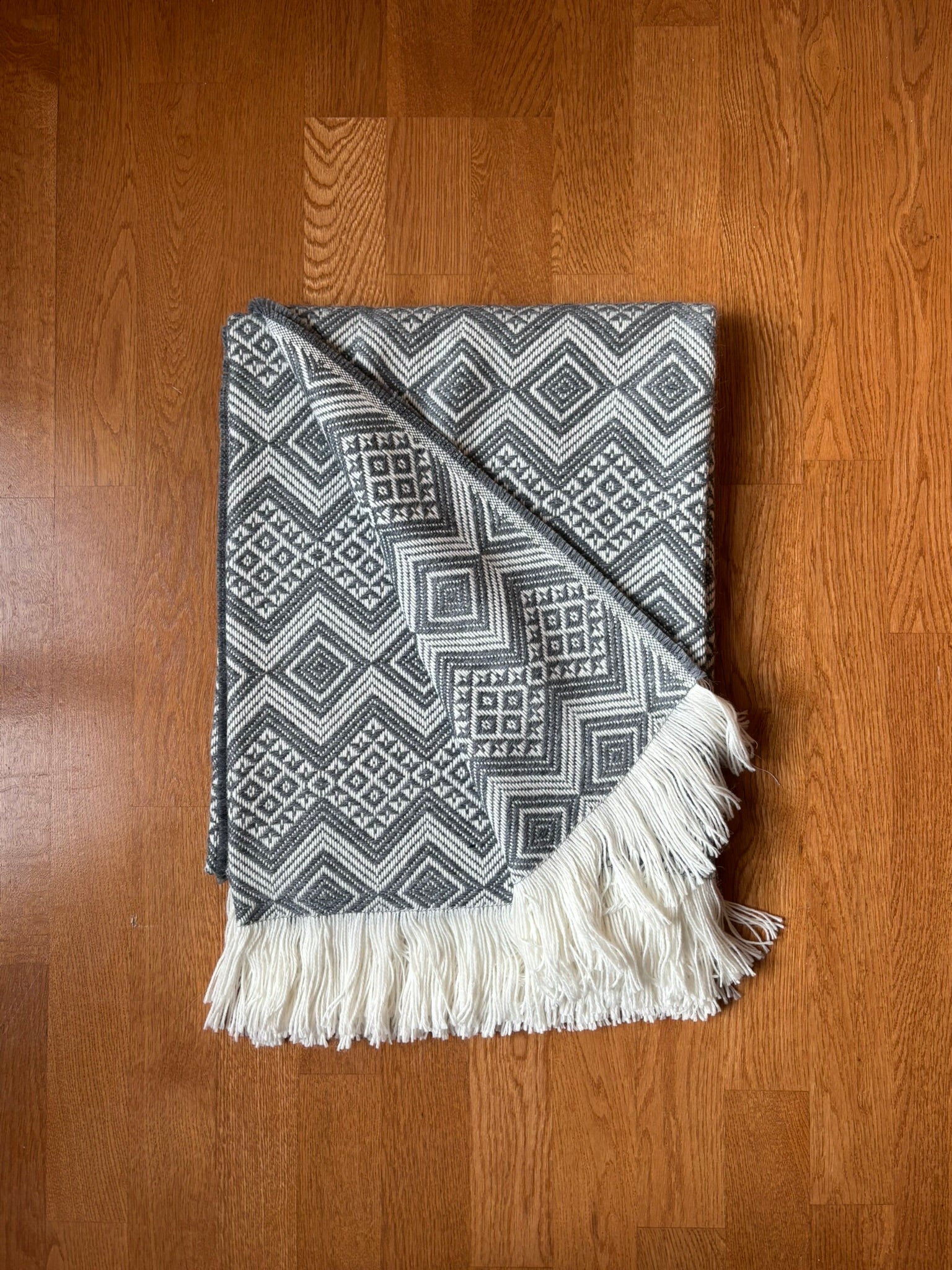 Silver woven blanket with a brand logo on a wooden surface