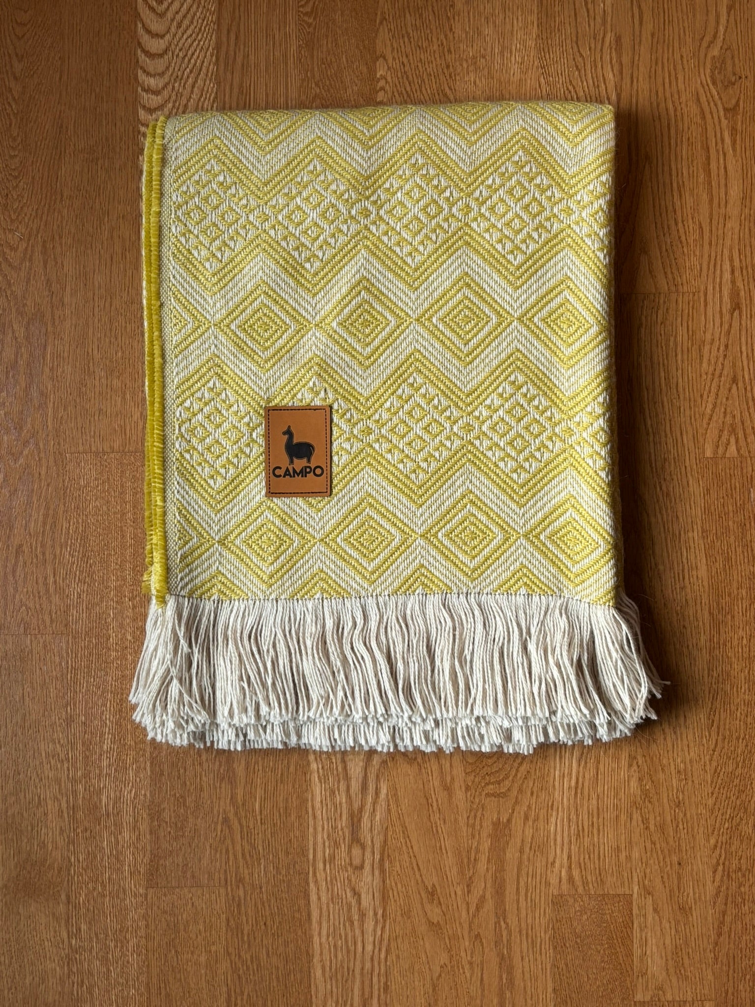 Yellow woven blanket with a brand logo on a wooden surface
