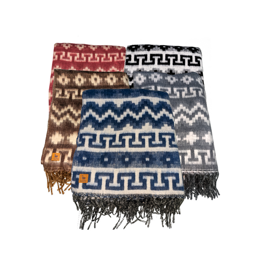 A collection of geometric patterned blankets in various colors with fringes, displayed on a neutral background.