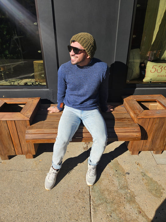Man sitting on a wooden bench wearing sunglasses and a blue sweater.
