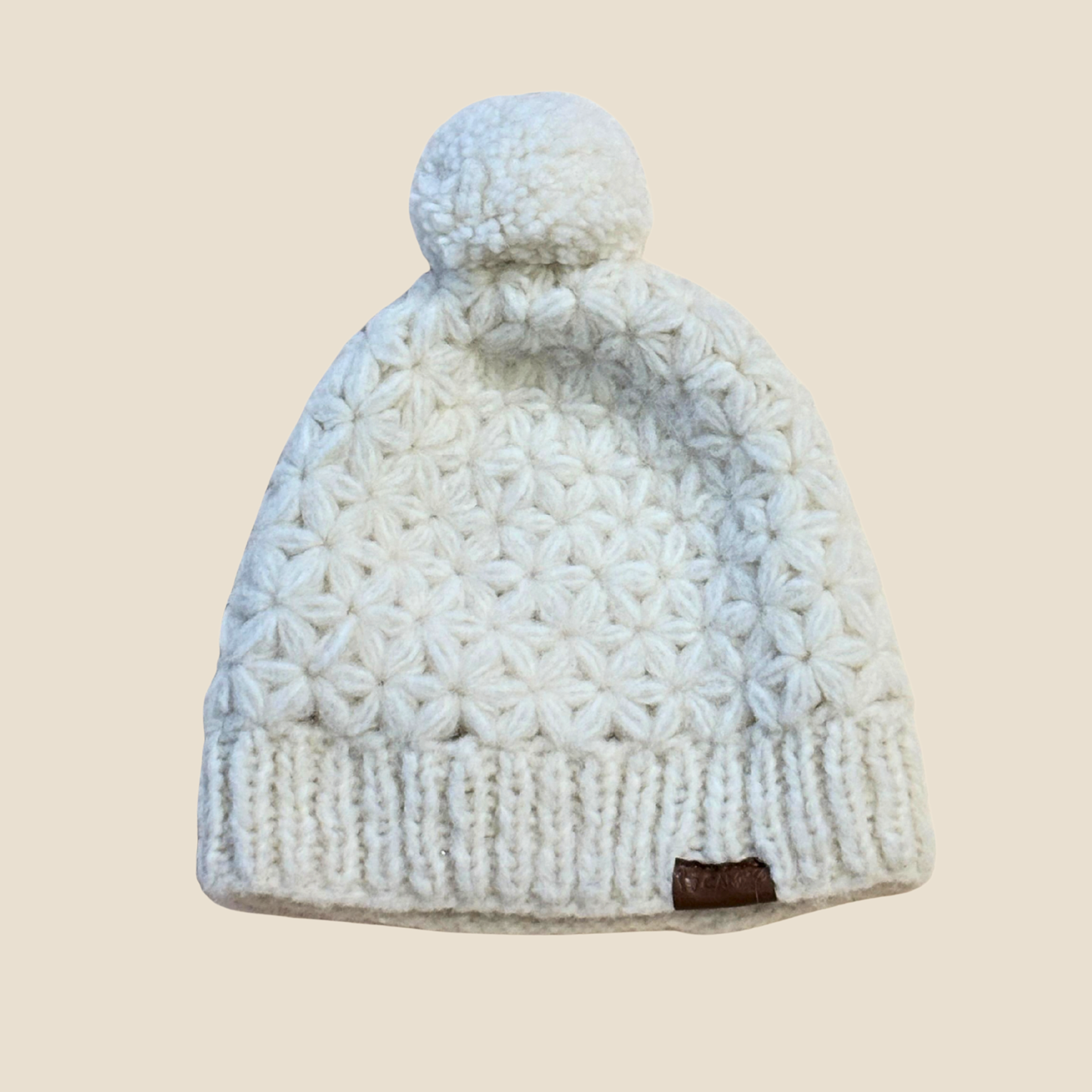 White knit beanie with a pom-pom on a beige background