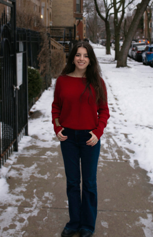 Woman in a red sweater and blue jeans standing on a snowy sidewalk.