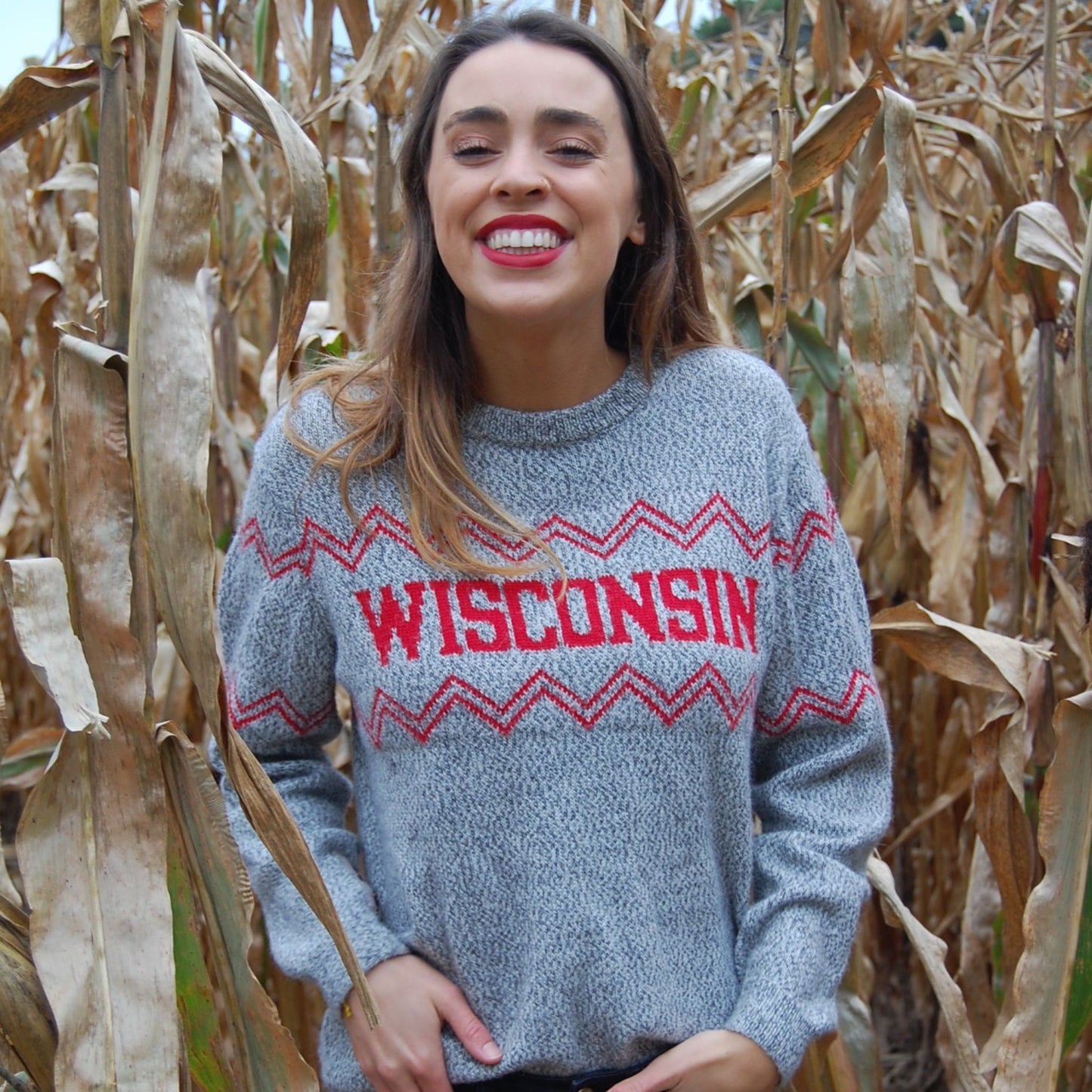 Woman wearing a gray sweater with 'Wisconsin' printed on it, standing in a cornfield.