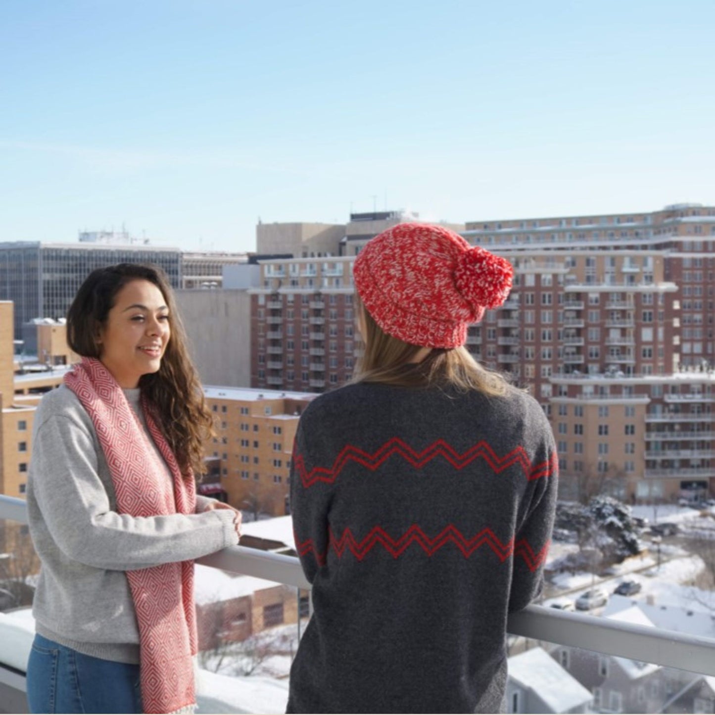 Two women on a rooftop wearing a wisconsin sweater with a cityscape in the background