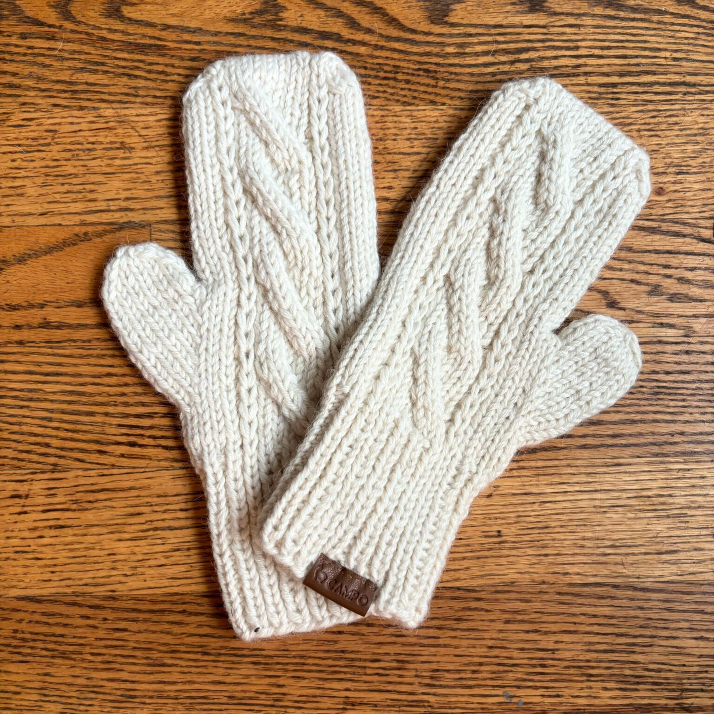 Pair of cream-colored knit mittens on a wooden surface