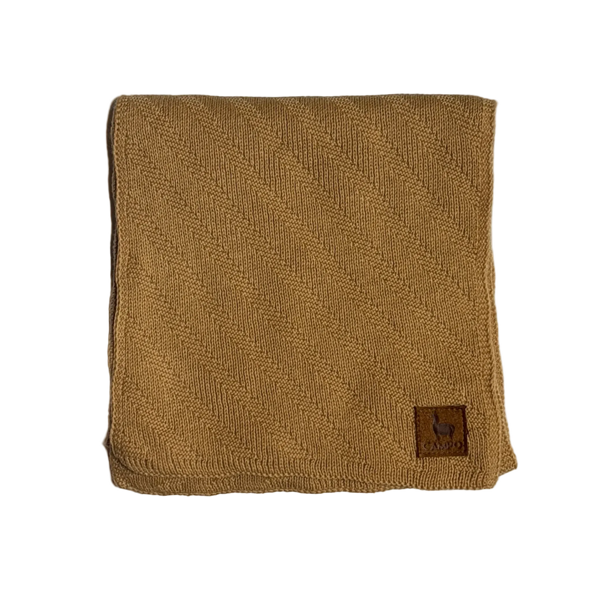 A folded tan woven blanket or throw with a small brown leather patch featuring a horse logo, displayed on a light textured background.