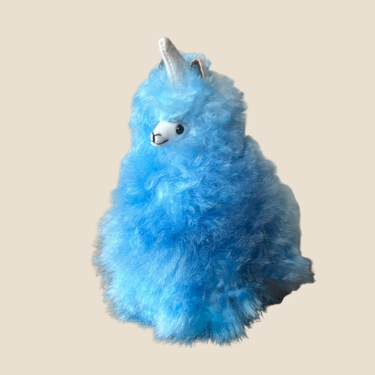 Blue plush toy with a unicorn horn on a beige background