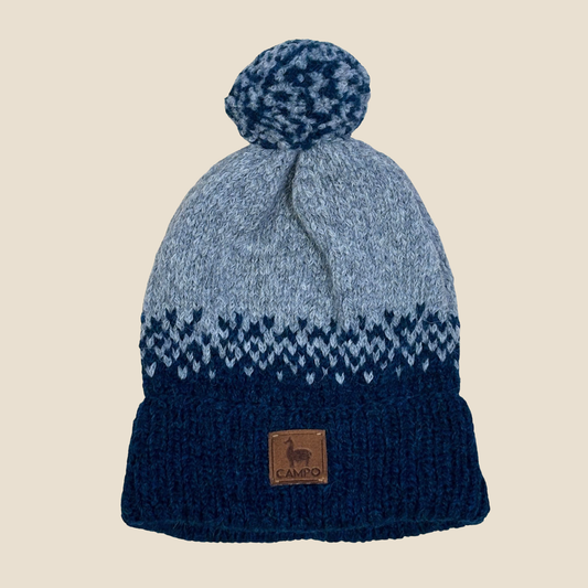Blue and gray knit beanie with a pom-pom on a beige background