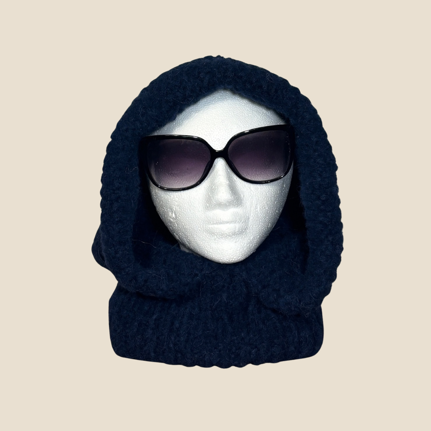 Navy blue knitted balaclava on a mannequin head with sunglasses against a beige background