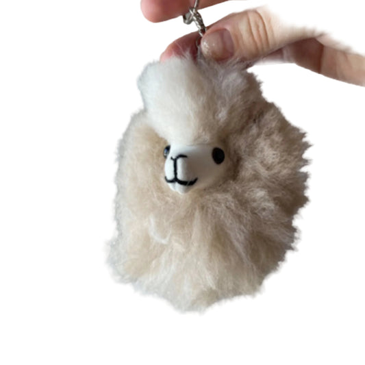 Fluffy keychain shaped like a alpaca held by a hand against a beige background