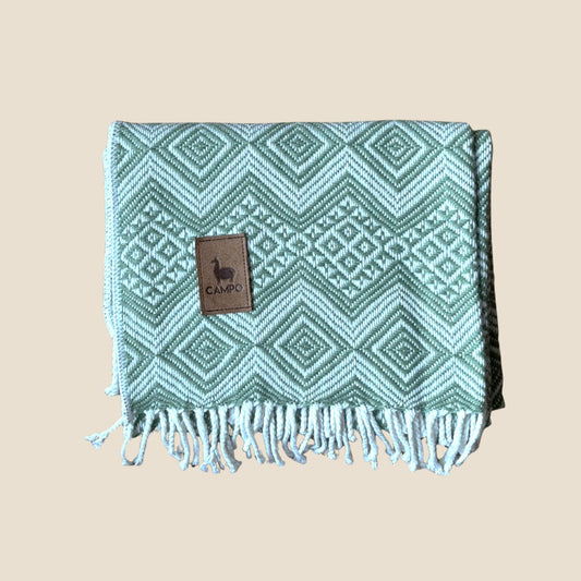 Sage patterned blanket with fringes and a brand label on a beige background
