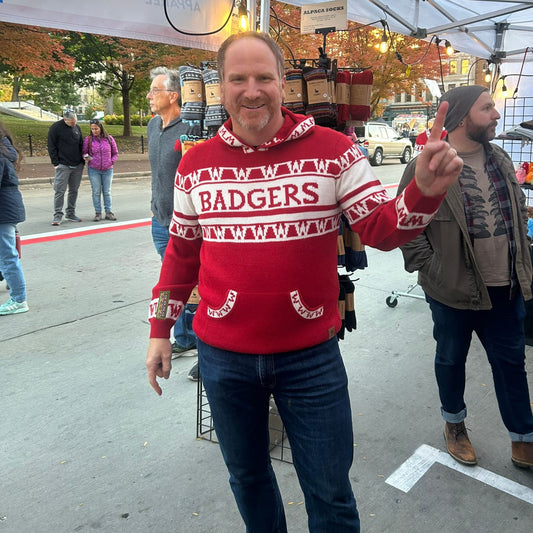 Man wearing a red 'Badgers' sweater outdoors with people and vehicles in the background.