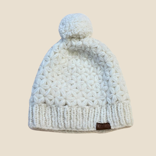 White knit beanie with a pom-pom on a beige background