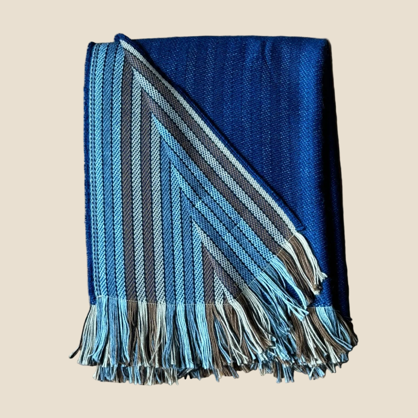 Blue and gray striped blanket with fringes on a beige background