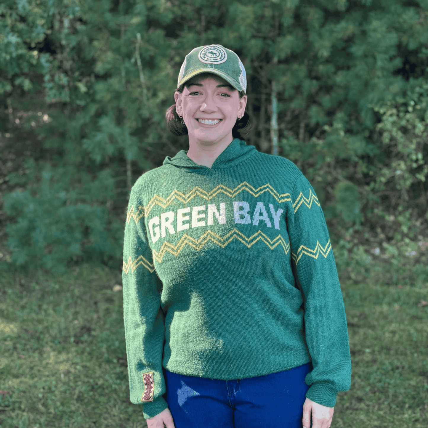 Person wearing a green 'Green Bay' sweater and cap outdoors