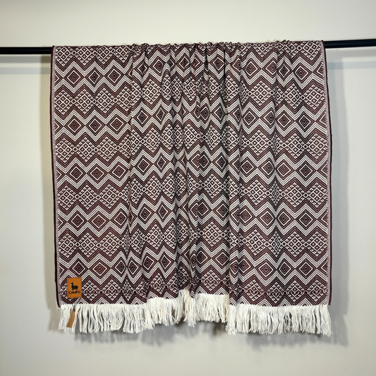 Patterned blanket with fringes on a black rod against a white wall