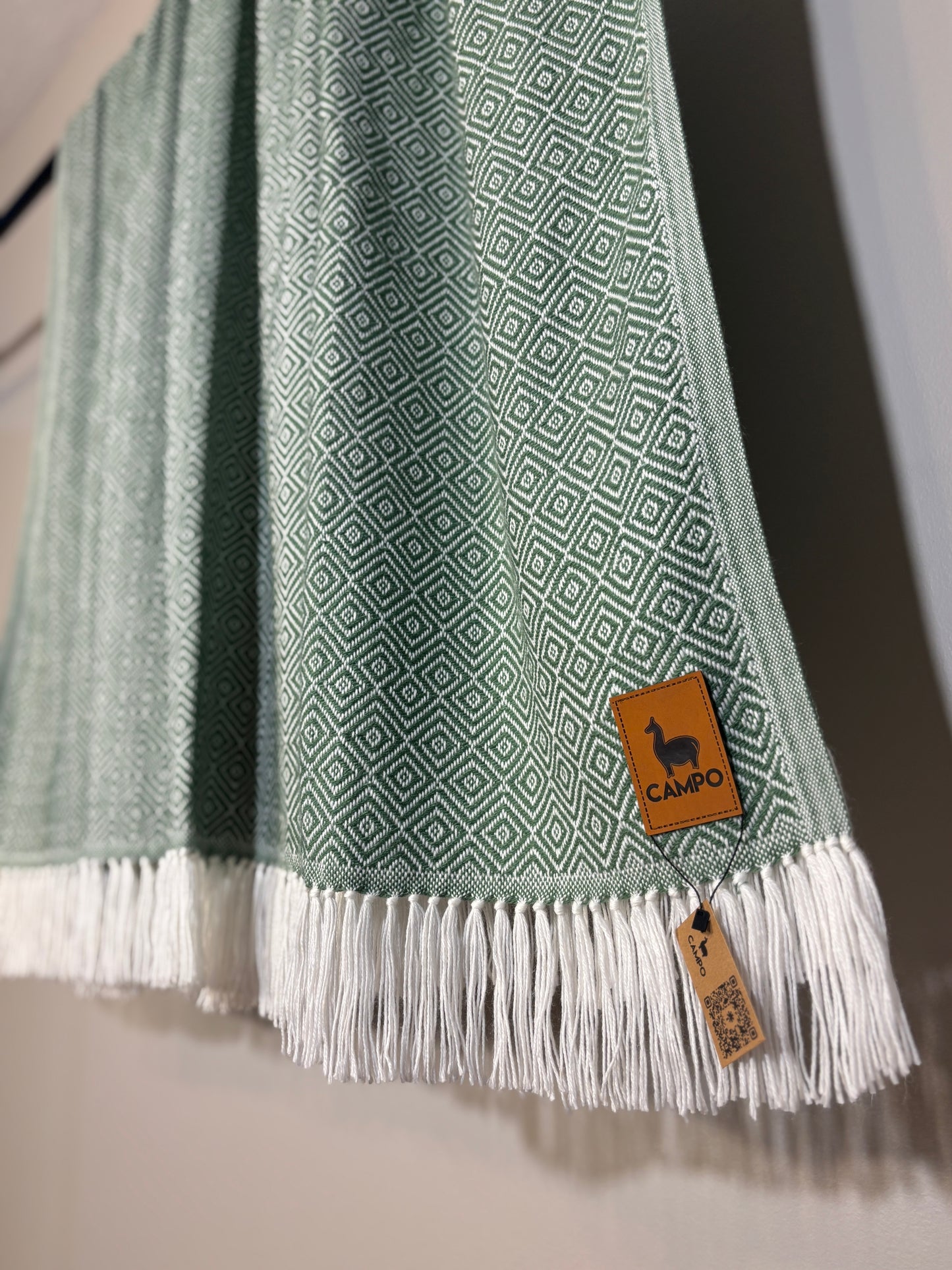 Green patterned scarf with white fringe and a brand tag on a neutral background