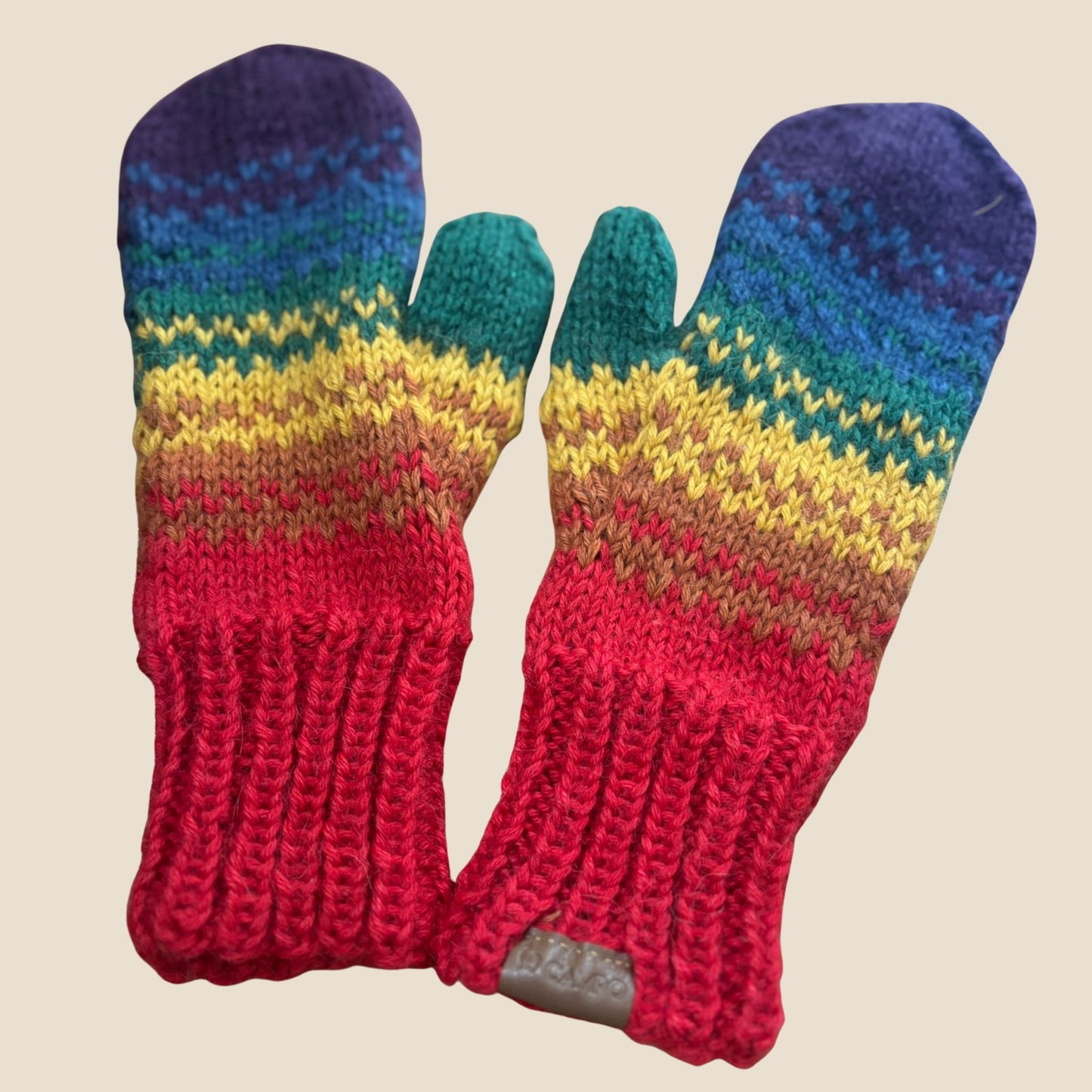 Pair of colorful knitted mittens with a rainbow pattern on a beige background