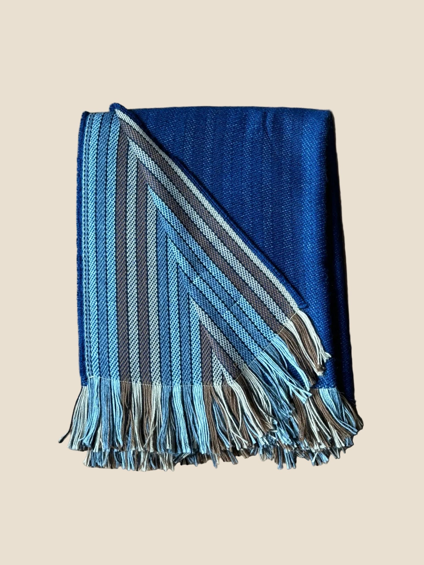 Blue and gray striped blanket with fringes on a wooden surface