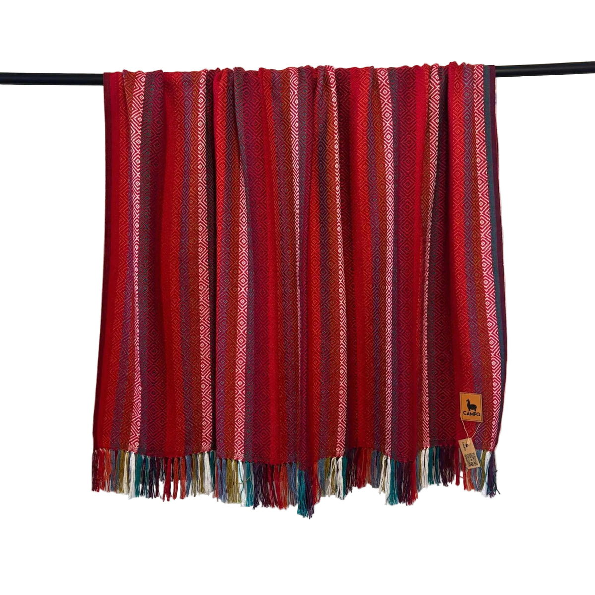 Red striped blanket with fringes on a black rod against a white wall