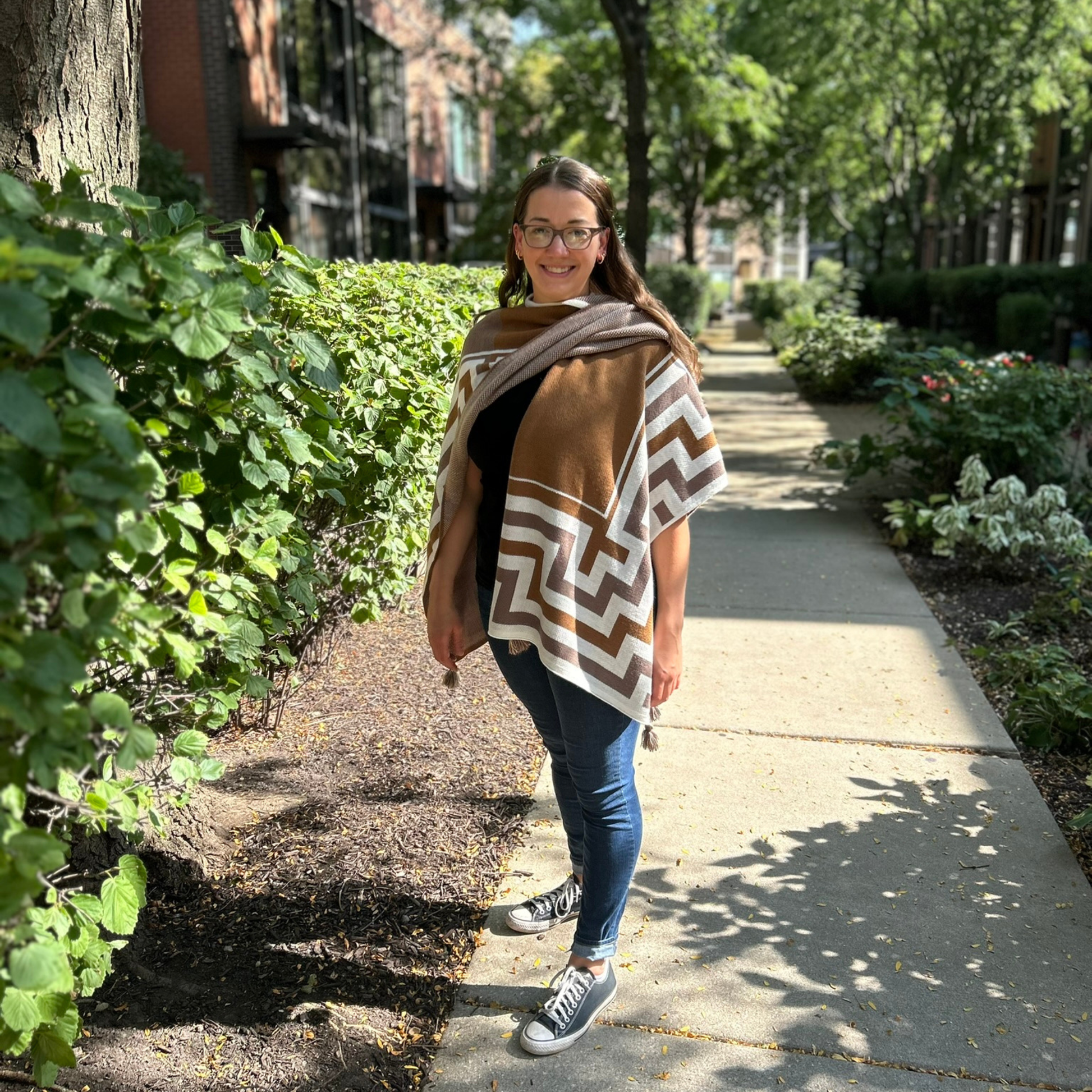 Woman wearing a natural brown Shawl on a sidewalk with greenery around