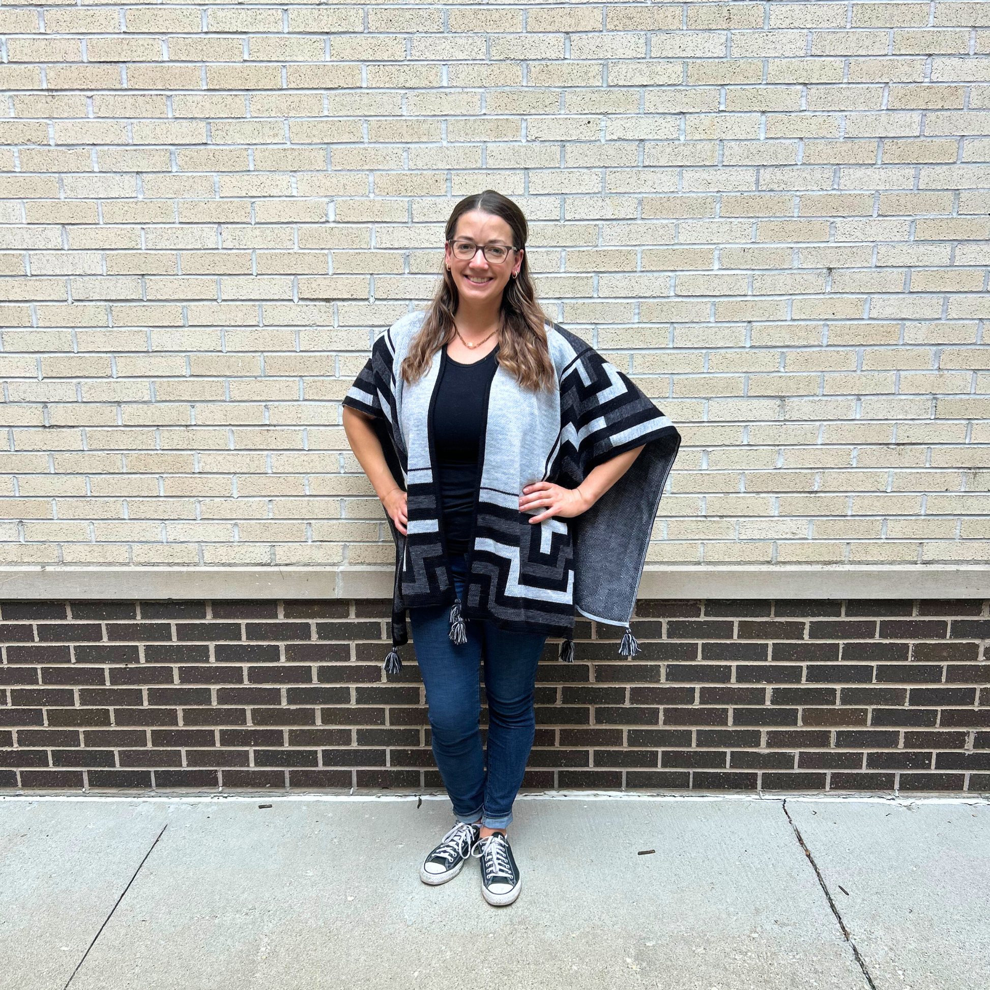 Woman wearing a patterned shawl standing against a brick wall.