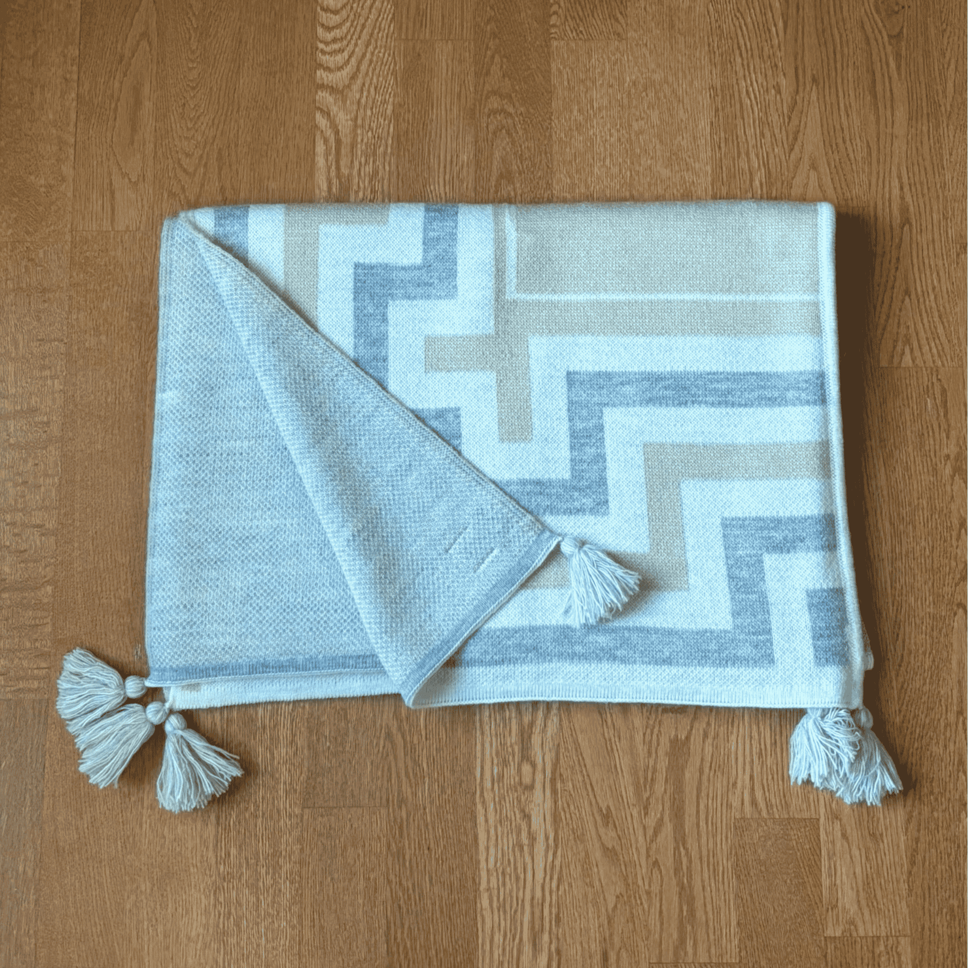 Shawl with geometric pattern and tassels on a wooden floor