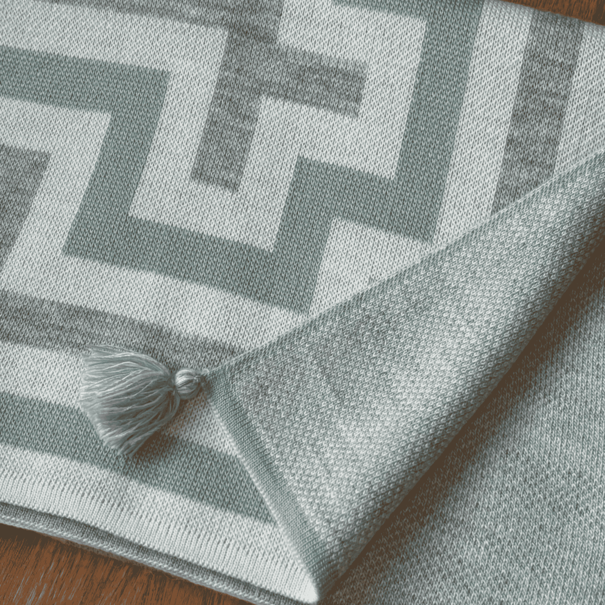 Gray patterned shawl with a tassel on a wooden surface
