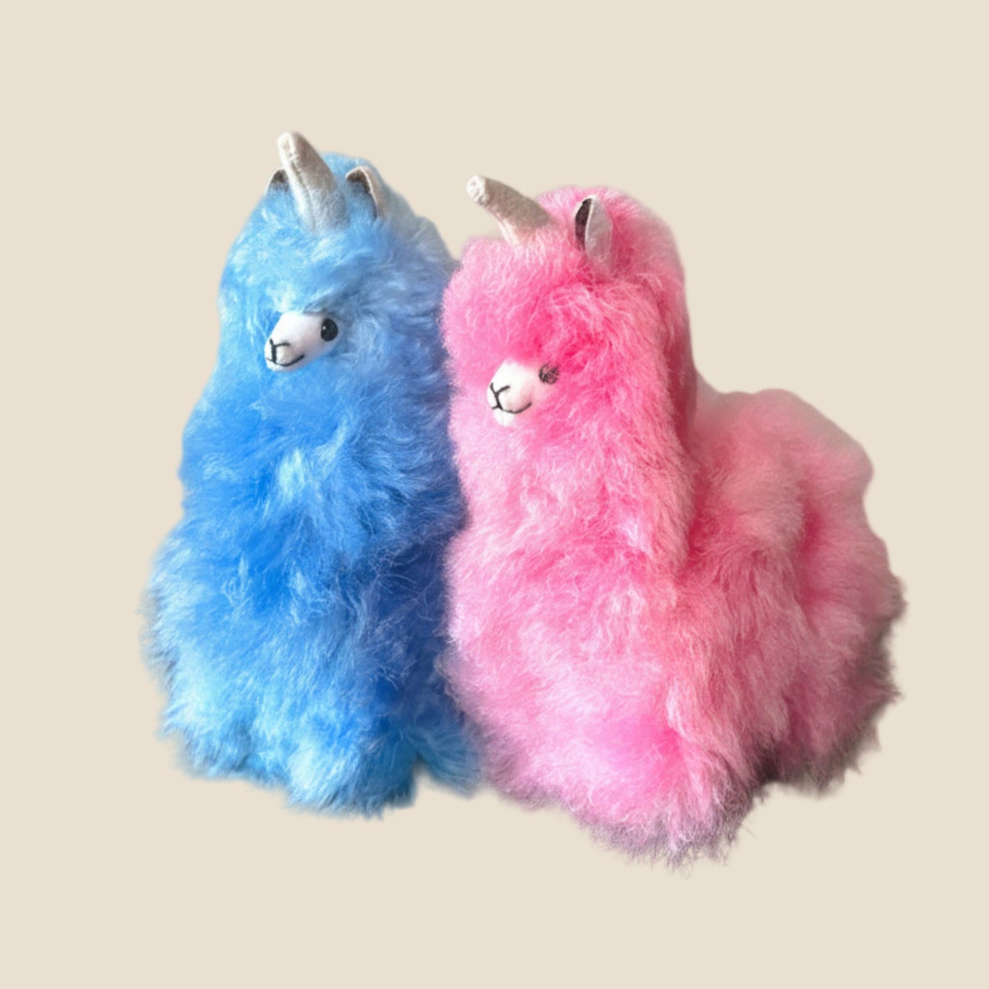 Two fluffy blue and pink unicorn toys on a beige background