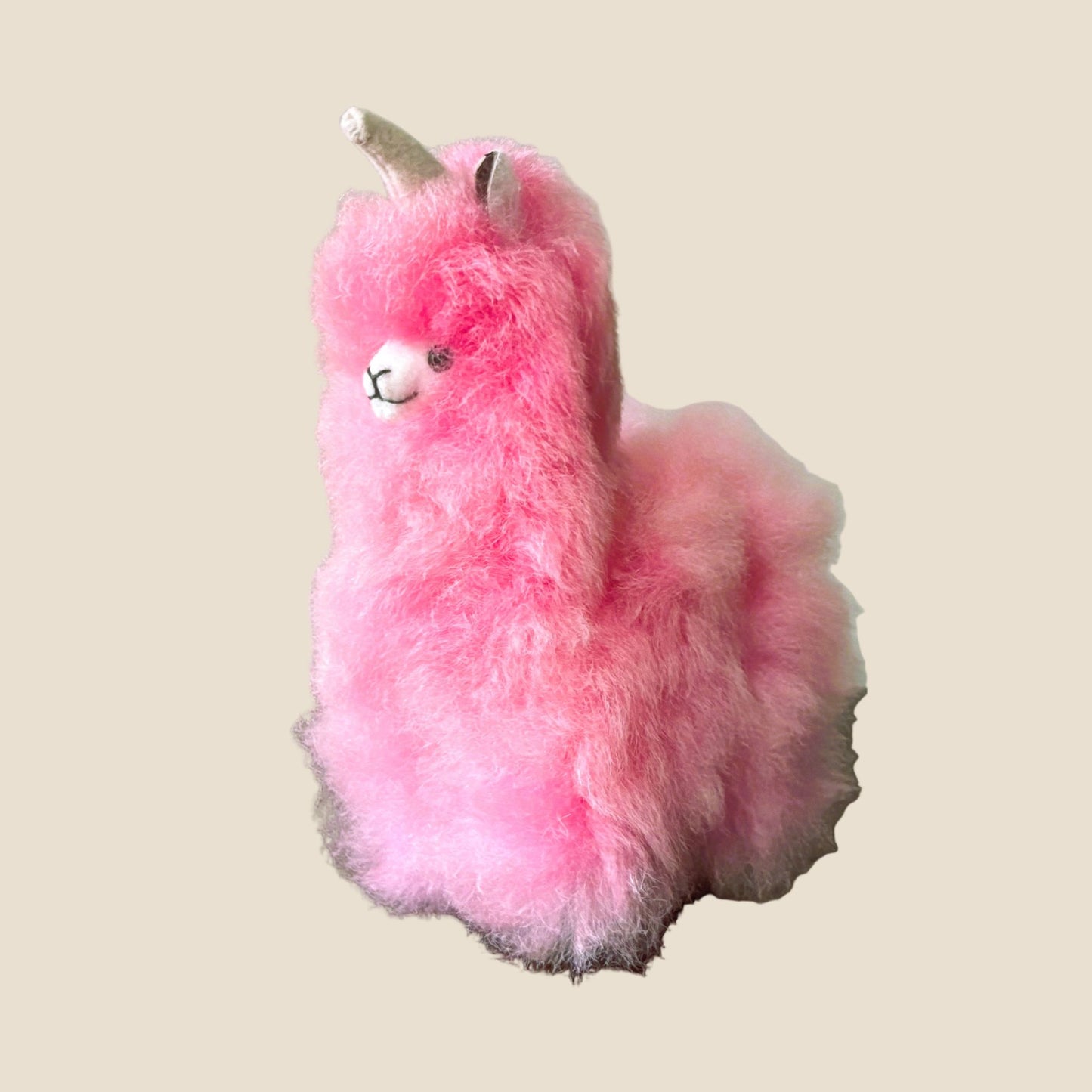 Pink plush toy resembling a alpaca on a beige background