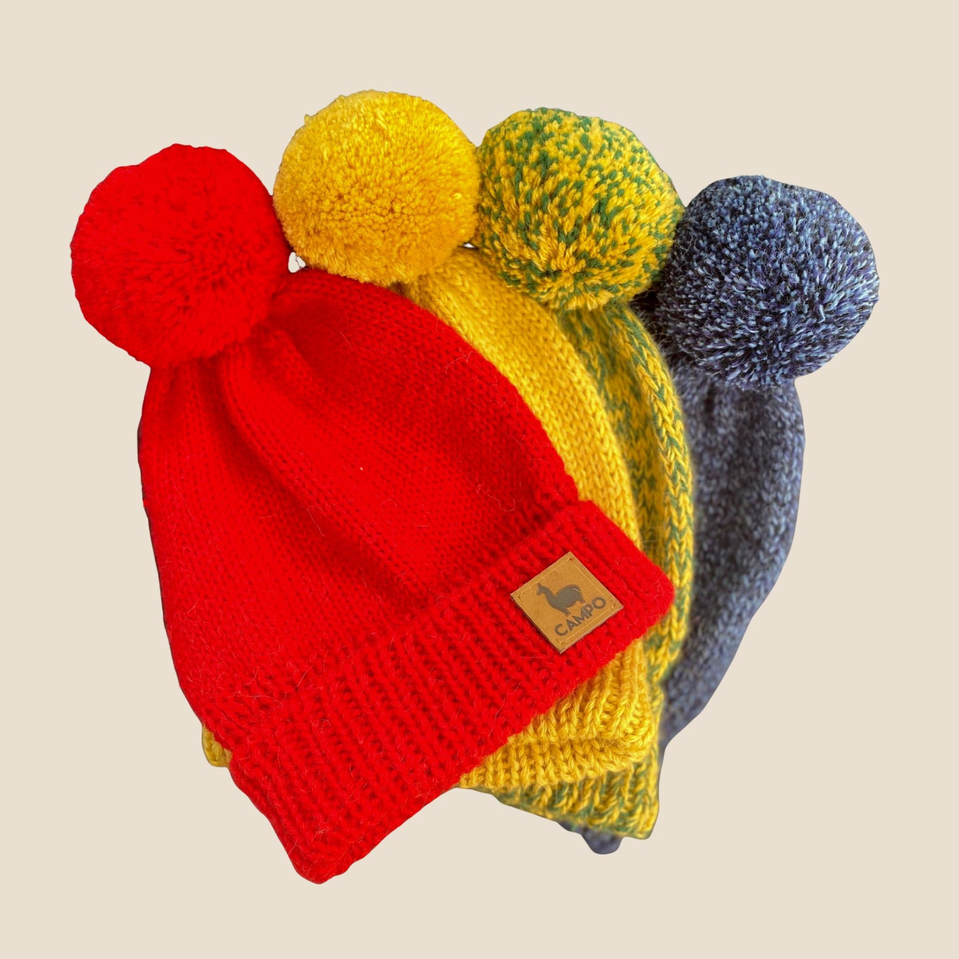 Four colorful knit beanie with pom-poms on a beige background