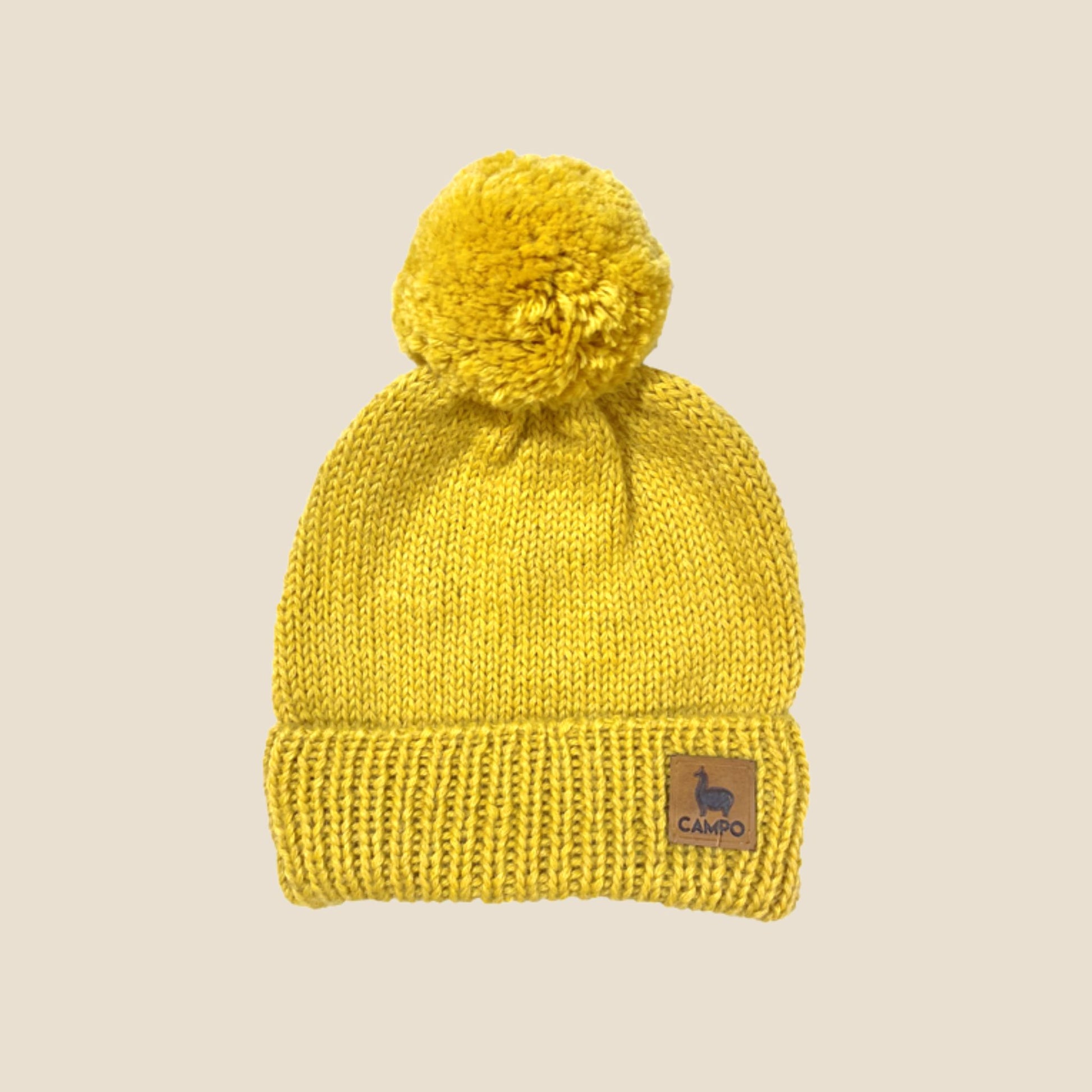 Mustard knit beanie with pom-pom on a beige background