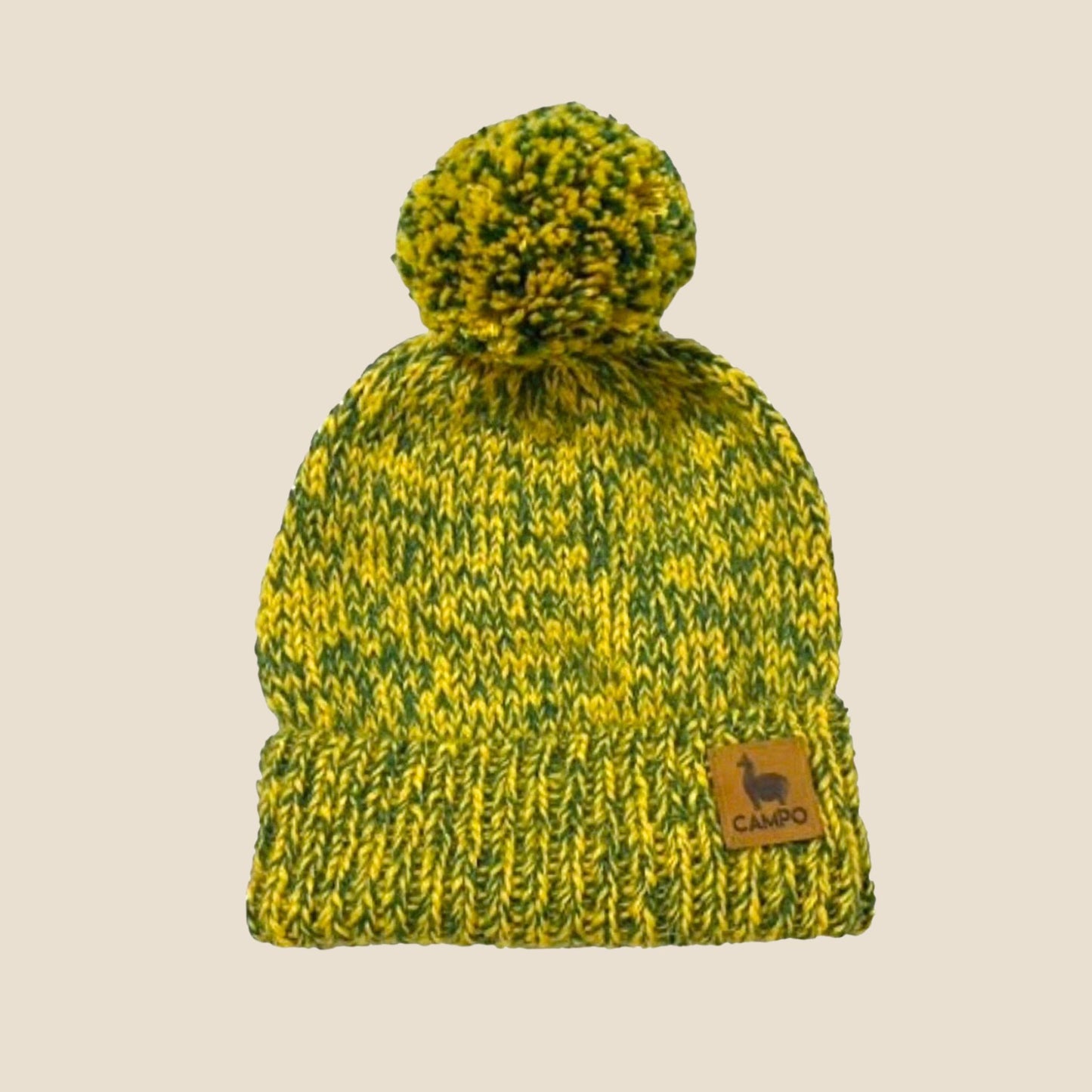 Green and yellow knitted beanie with a pom-pom on a beige background