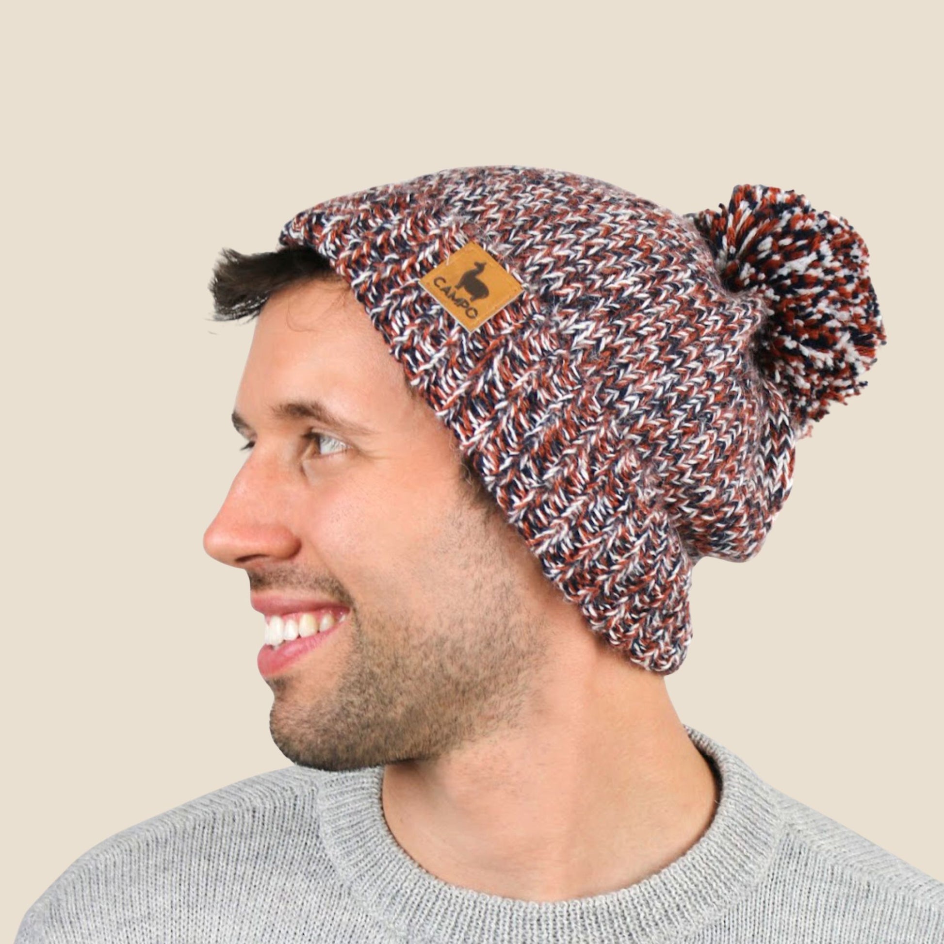 Man wearing a patterned beanie with a pom-pom on a beige background