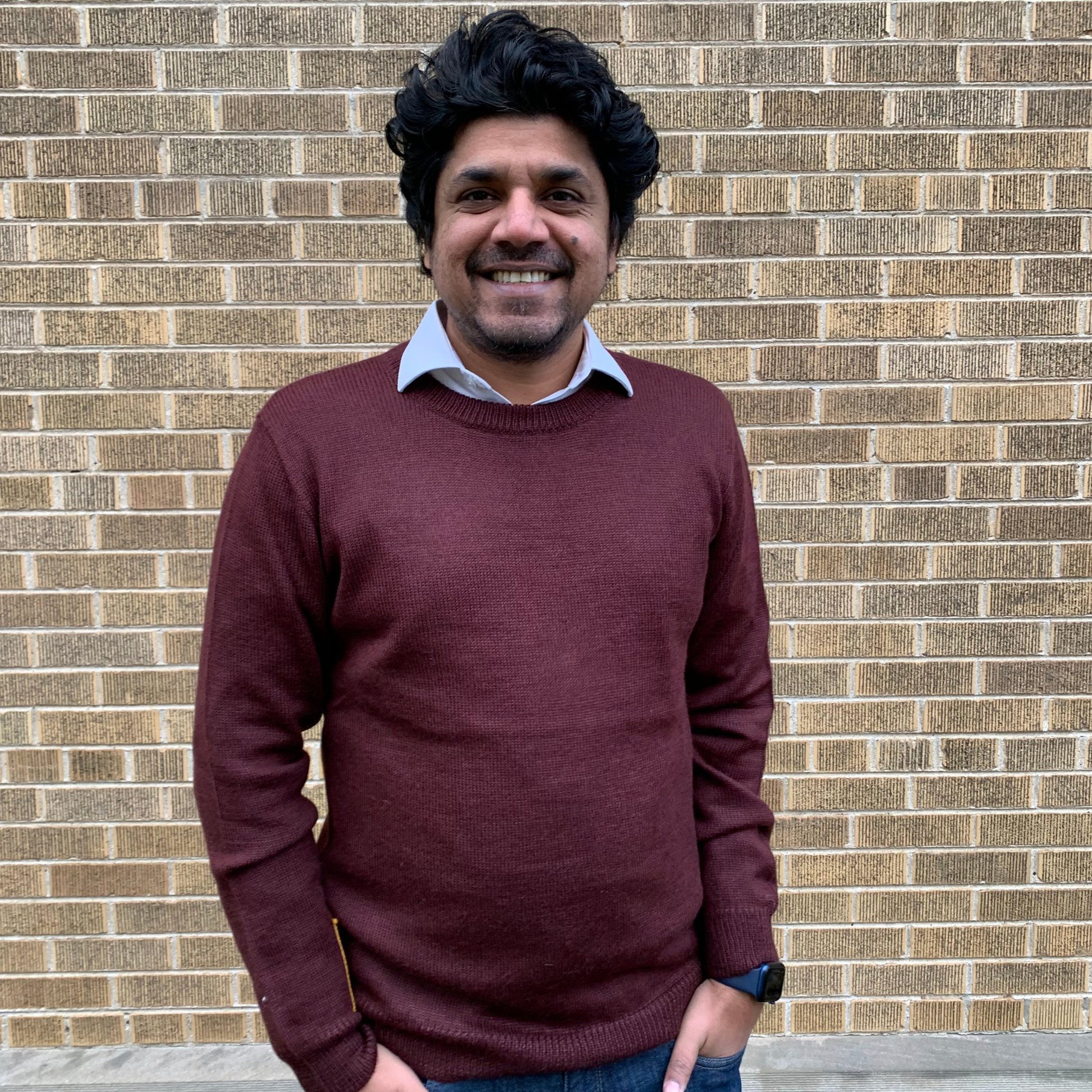 Man wearing a maroon sweater in front of a brick wall