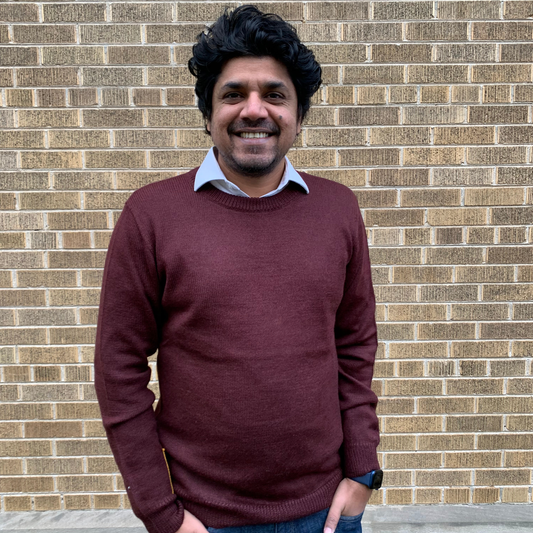 Man wearing a maroon sweater in front of a brick wall
