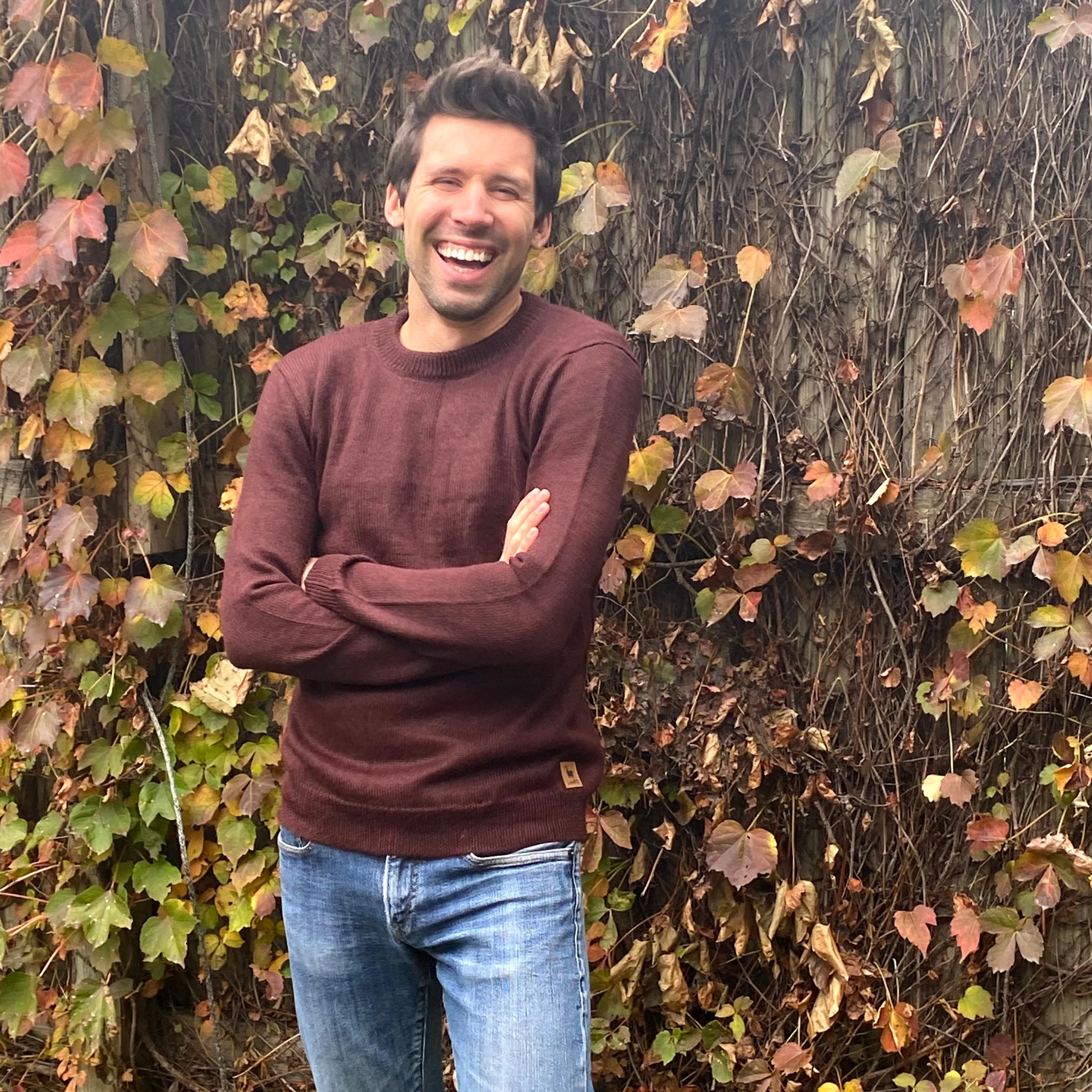 Man in a maroon sweater standing in front of a leafy wall